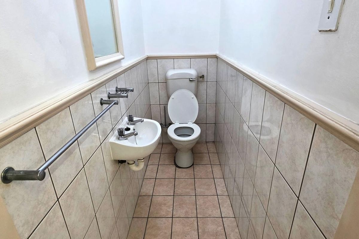 A compact guest bathroom featuring tiled walls and flooring, a wall-mounted basin, and a standard toilet.