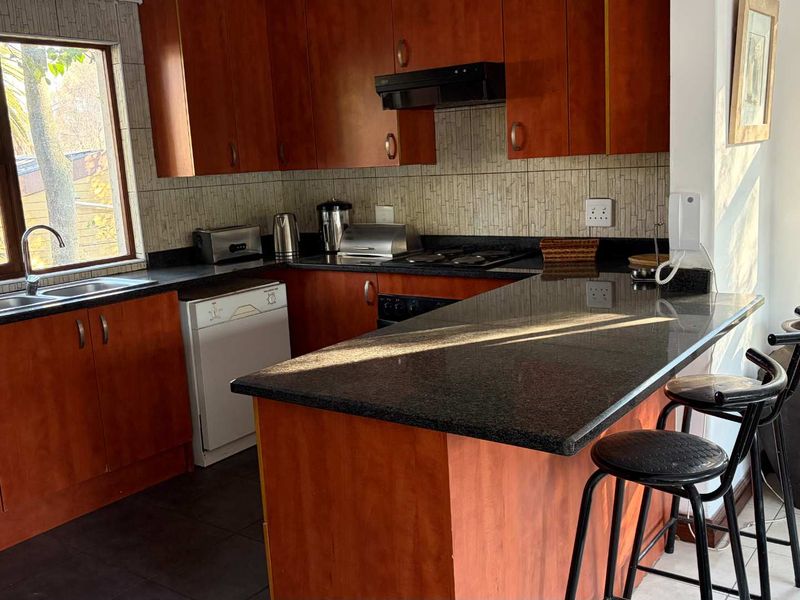 A functional kitchen featuring warm-toned wooden cabinetry, dark granite countertops, a breakfast bar, and large windows providing ample natural light.