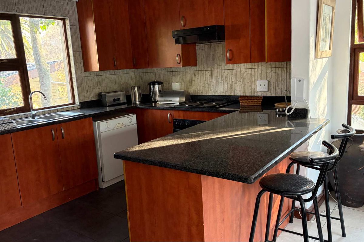 A functional kitchen featuring warm-toned wooden cabinetry, dark granite countertops, a breakfast bar, and large windows providing ample natural light.
