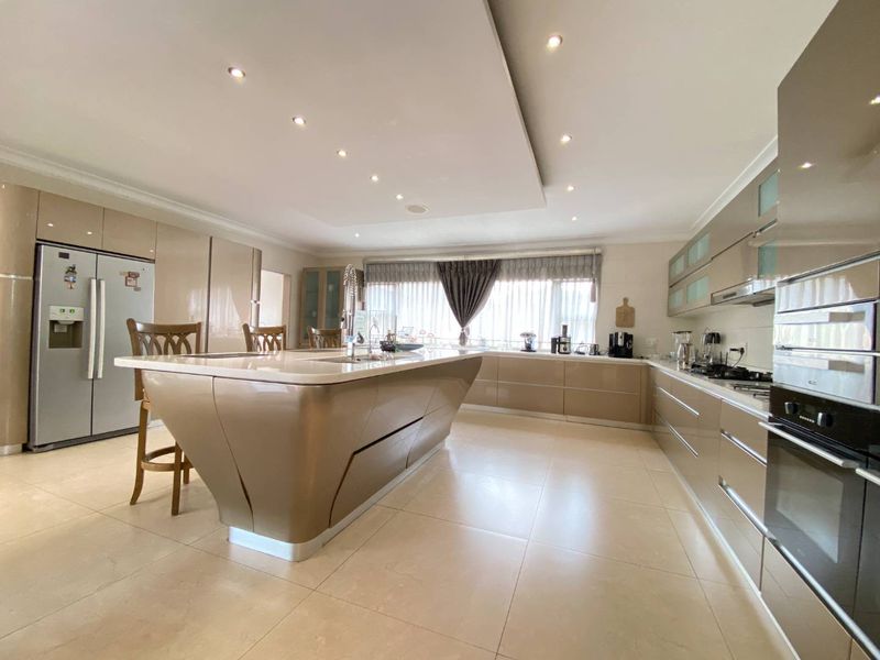 Modern, spacious kitchen featuring a large central island, high-gloss cabinetry, stone countertops, built-in appliances, and recessed ceiling lighting.