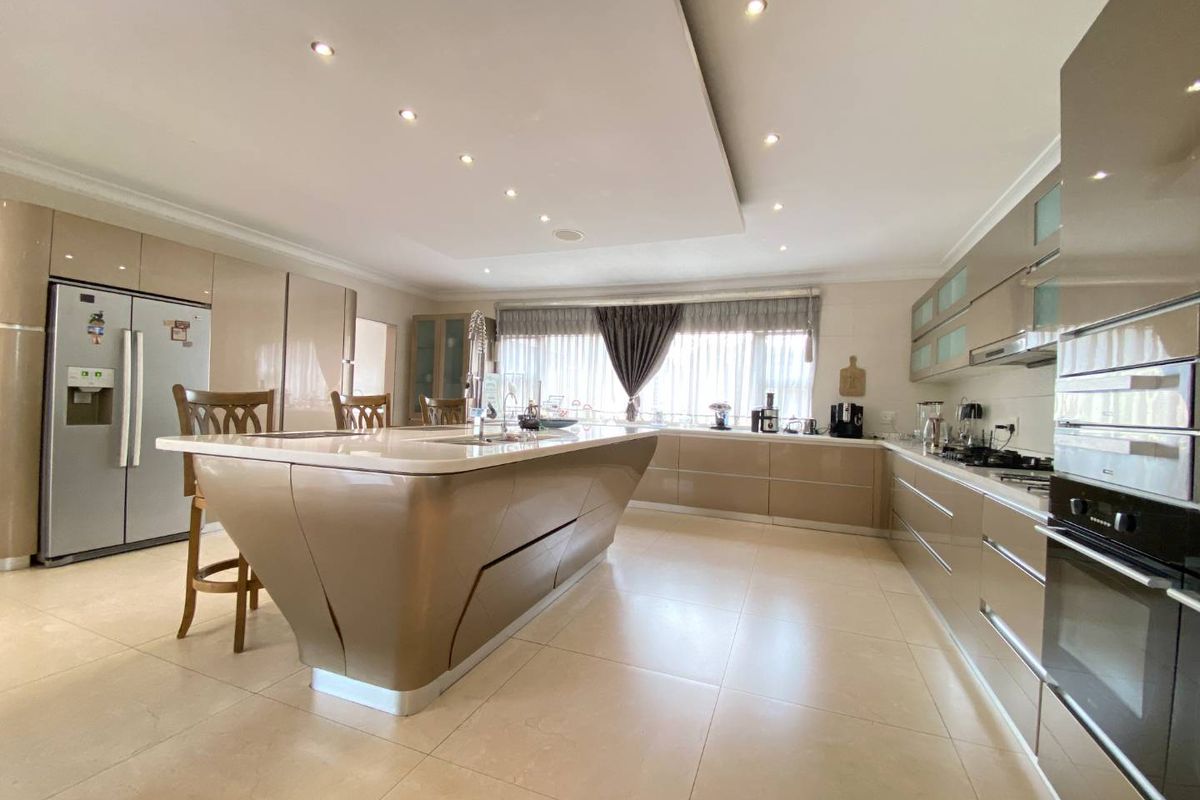 Modern, spacious kitchen featuring a large central island, high-gloss cabinetry, stone countertops, built-in appliances, and recessed ceiling lighting.