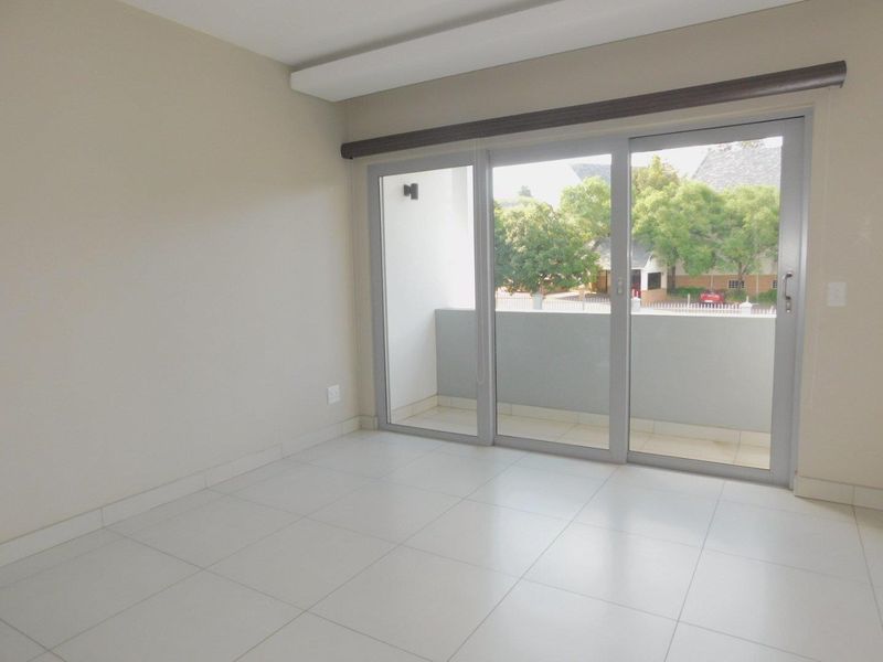 A bright, empty bedroom featuring neutral tiled flooring and large sliding glass doors that provide direct access to a private balcony.