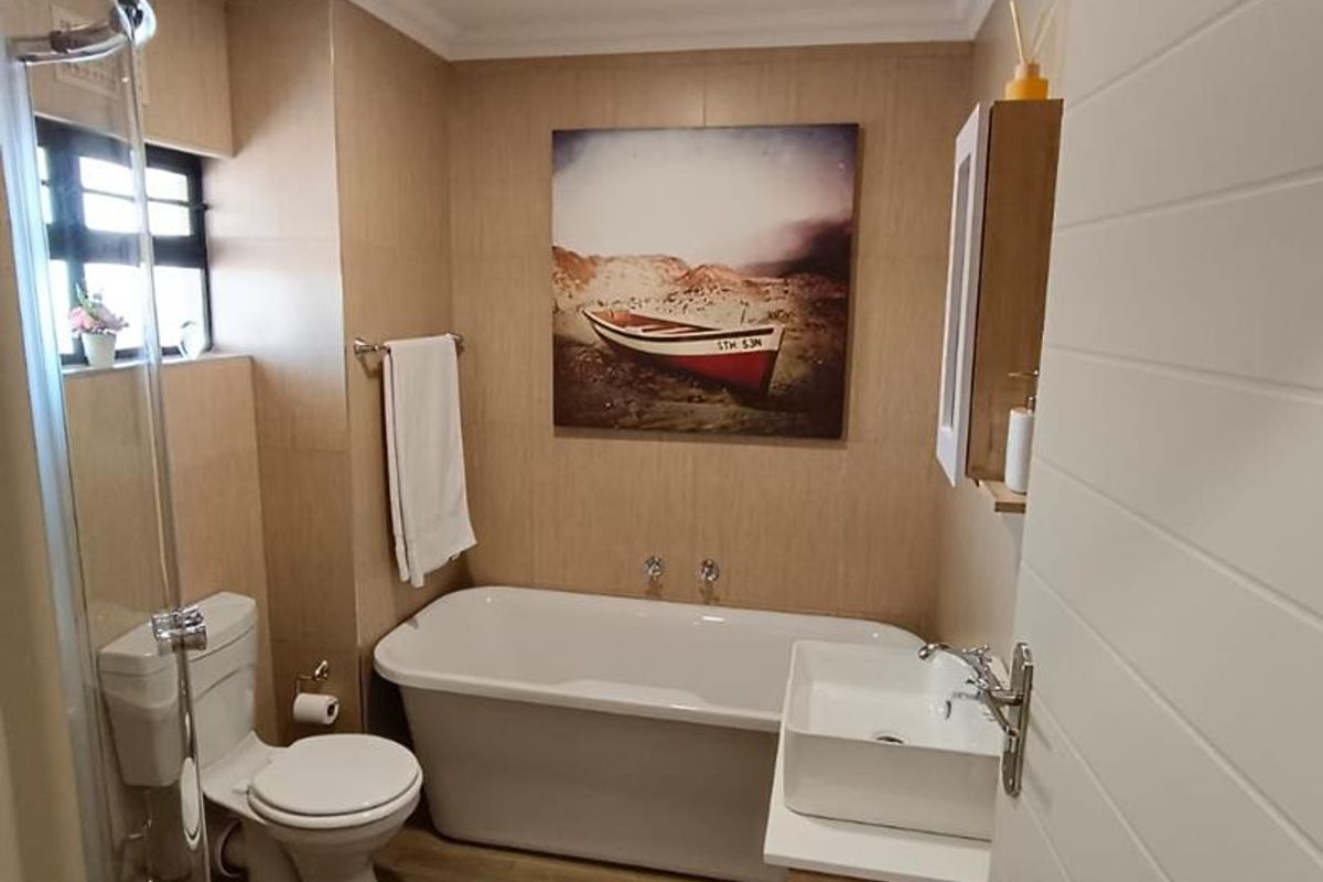 A well-maintained bathroom featuring a freestanding bathtub, a separate glass-enclosed shower, a modern vanity basin, and neutral wall tiling.