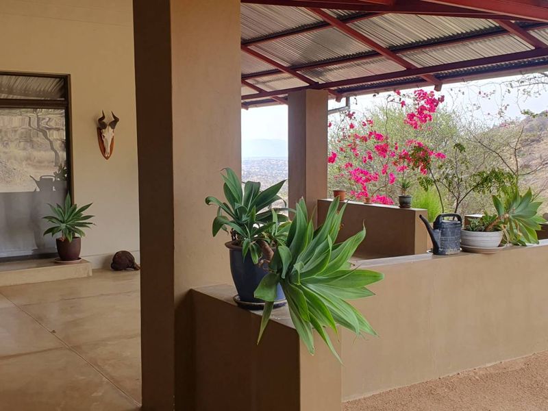 A covered outdoor patio area featuring concrete pillars, a corrugated metal roof, and a sliding glass door entrance with scenic views.