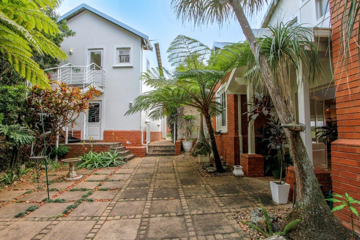 A charming rear courtyard featuring paved pathways, established garden greenery, and a multi-level building facade with a metal spiral staircase.