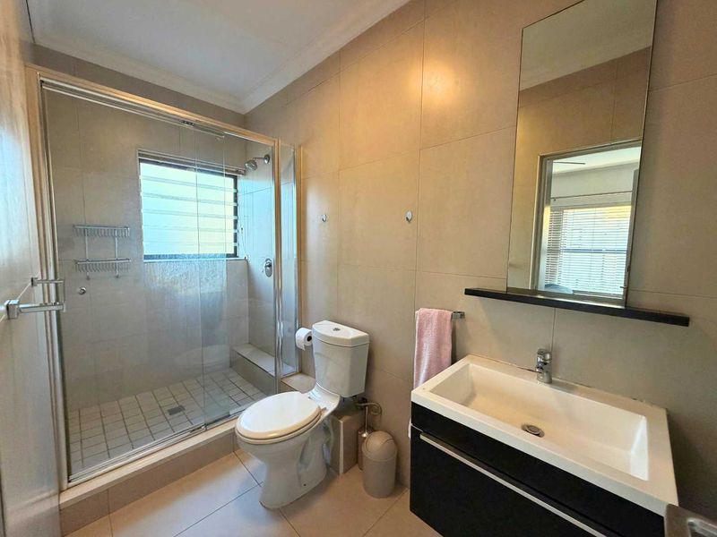 A modern bathroom featuring a glass-enclosed shower, a wall-mounted vanity with a basin, and neutral wall tiling.