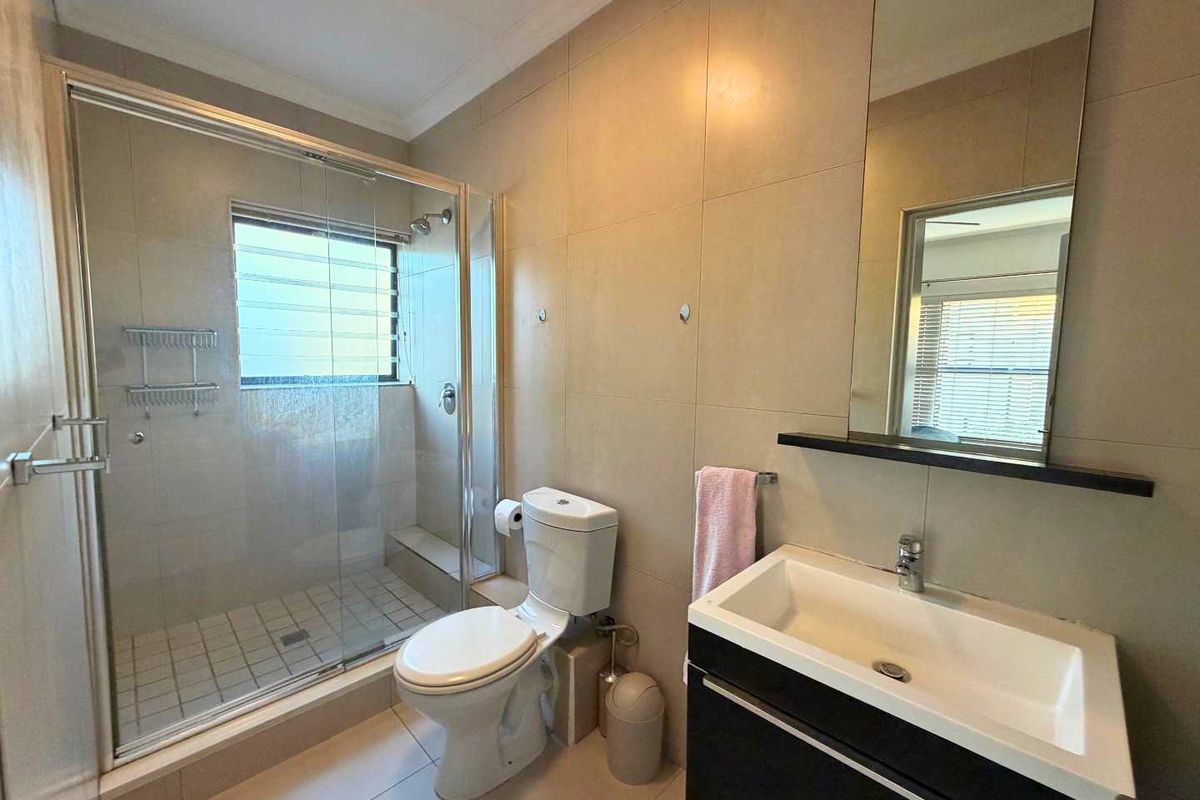 A modern bathroom featuring a glass-enclosed shower, a wall-mounted vanity with a basin, and neutral wall tiling.