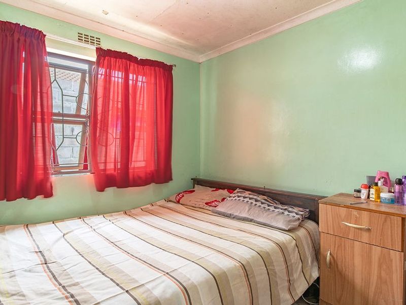 A bedroom featuring a window with security bars and coving, currently showing signs of wear on the ceiling.