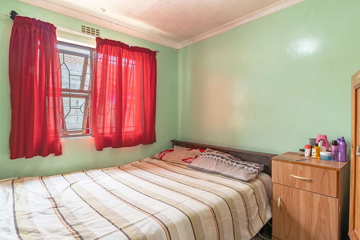 A bedroom featuring a window with security bars and coving, currently showing signs of wear on the ceiling.