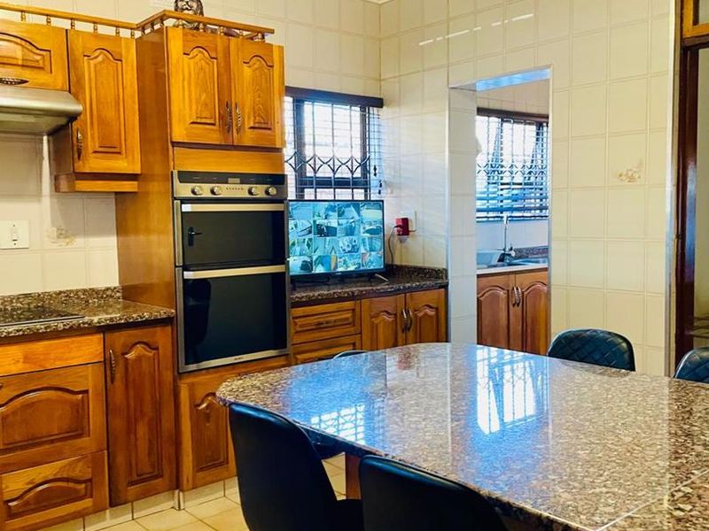A functional kitchen featuring traditional wooden cabinetry, granite countertops, a built-in double oven, and tiled finishes, with an adjacent scullery area visible.