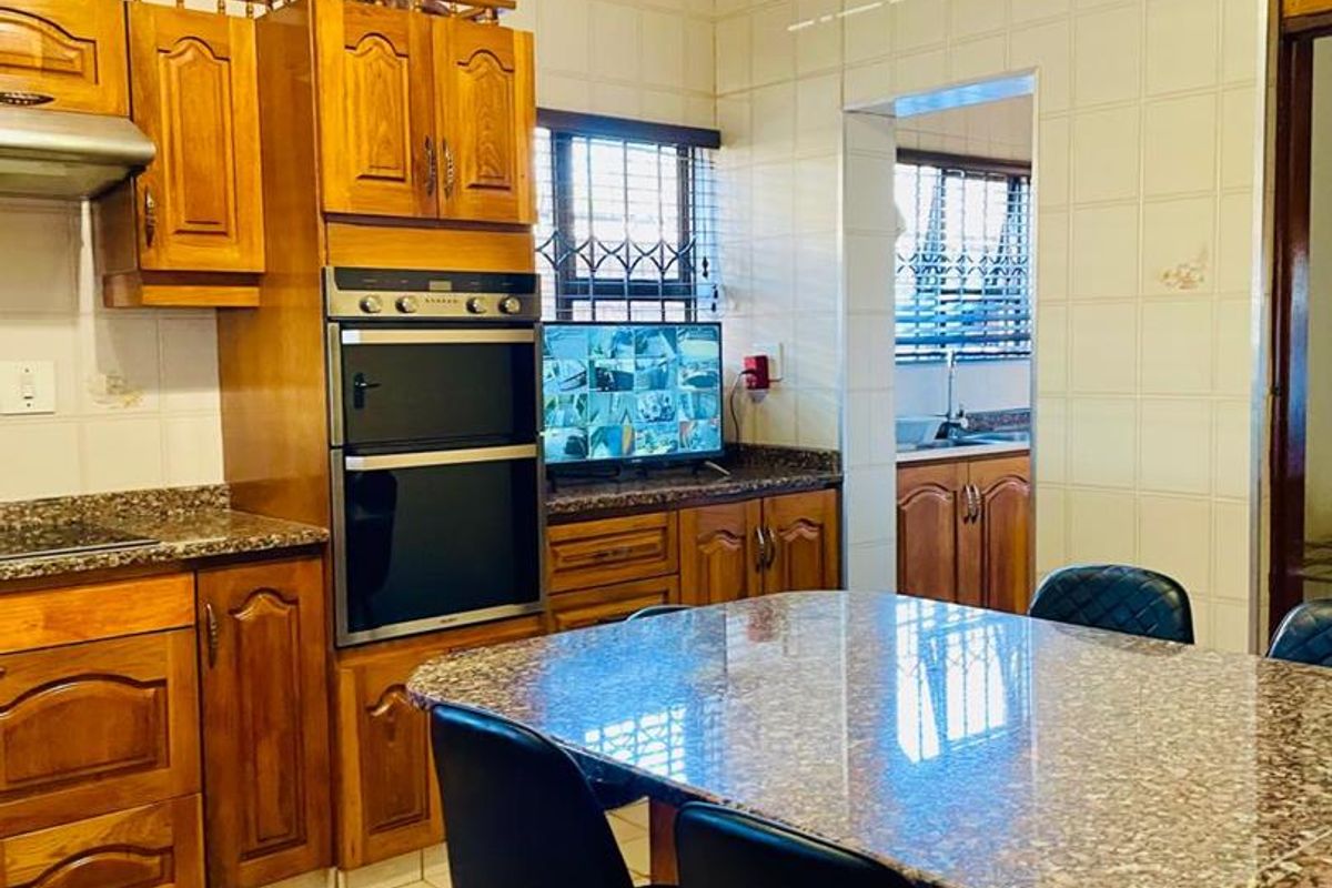 A functional kitchen featuring traditional wooden cabinetry, granite countertops, a built-in double oven, and tiled finishes, with an adjacent scullery area visible.