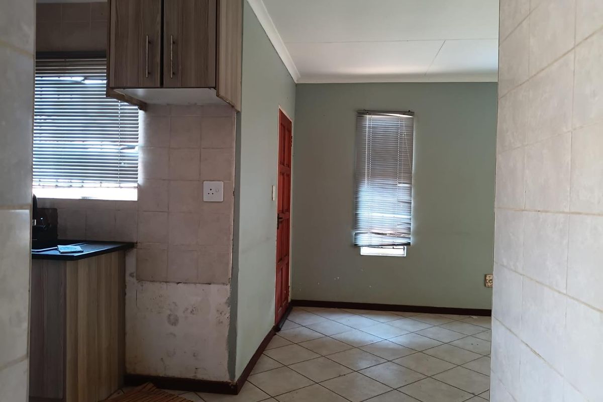 A compact kitchen area featuring tiled flooring, built-in cabinetry, and tiled splashbacks, currently requiring some cosmetic repairs and updates to the wall finishes.