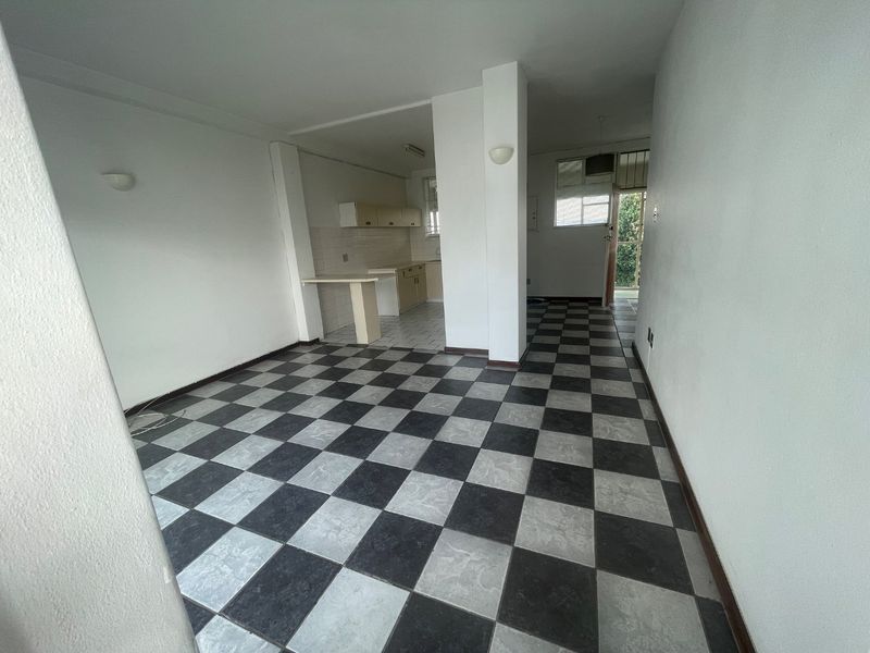 An empty open-plan living and kitchen area featuring a checkerboard tiled floor, built-in kitchen cabinetry, and a breakfast counter.