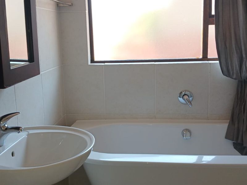 A functional bathroom featuring a white bathtub, a modern basin with a mixer tap, and tiled wall finishes.