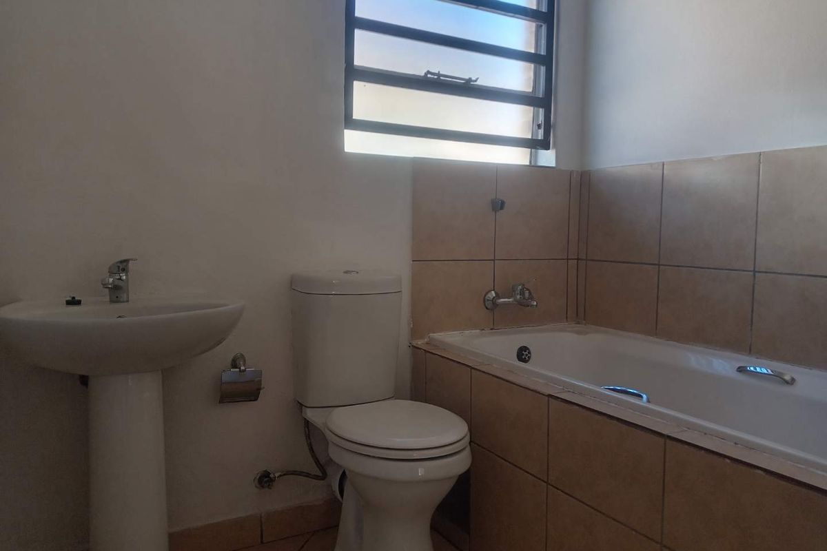 A functional bathroom featuring a pedestal basin, a standard toilet, and a tiled bathtub with a wall-mounted faucet and louvered window.