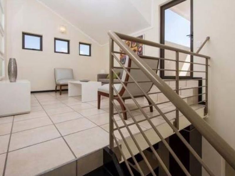 A bright living area featuring tiled flooring, a vaulted ceiling, and a modern metal balustrade overlooking the lower level.