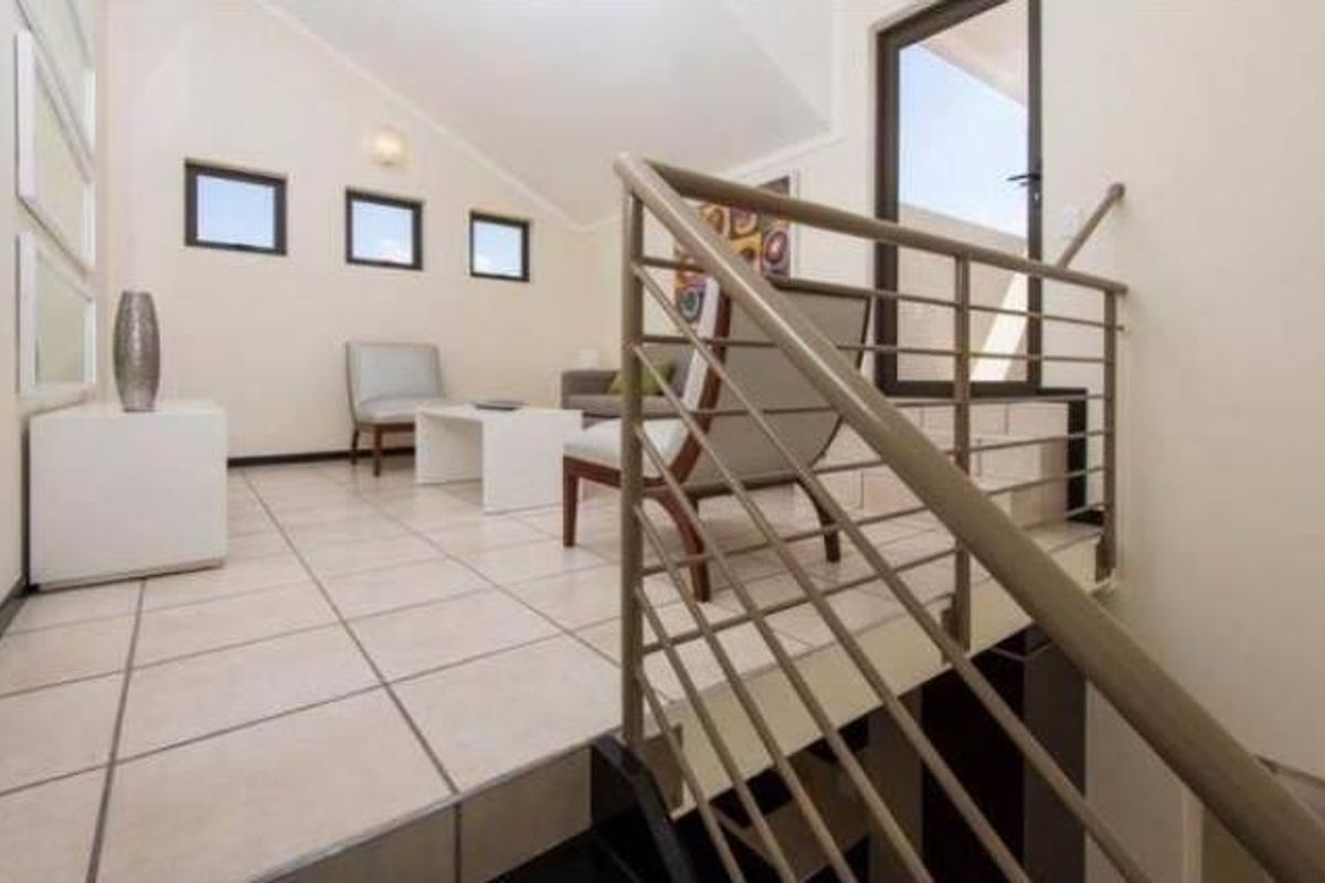 A bright living area featuring tiled flooring, a vaulted ceiling, and a modern metal balustrade overlooking the lower level.