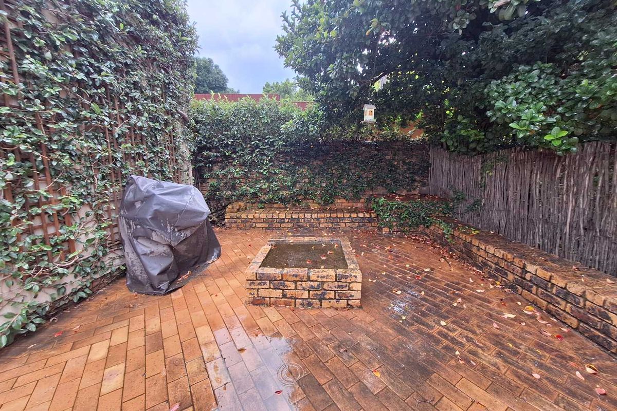 A private rear courtyard featuring brick paving, a built-in brick fire pit, and established climbing greenery along the perimeter walls.