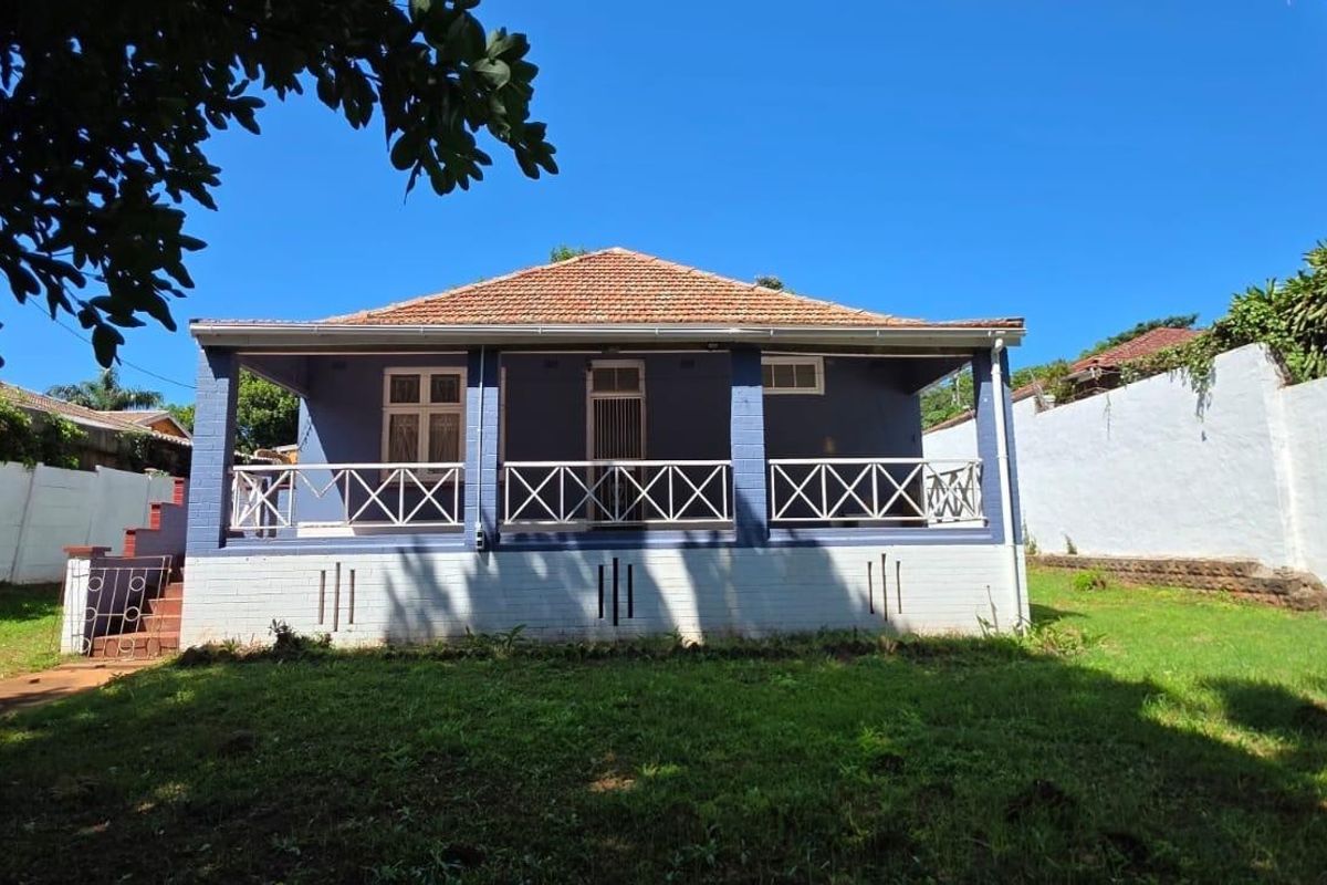 Rear view of a detached house featuring a covered veranda, tiled roof, and surrounding garden space with perimeter boundary walls.