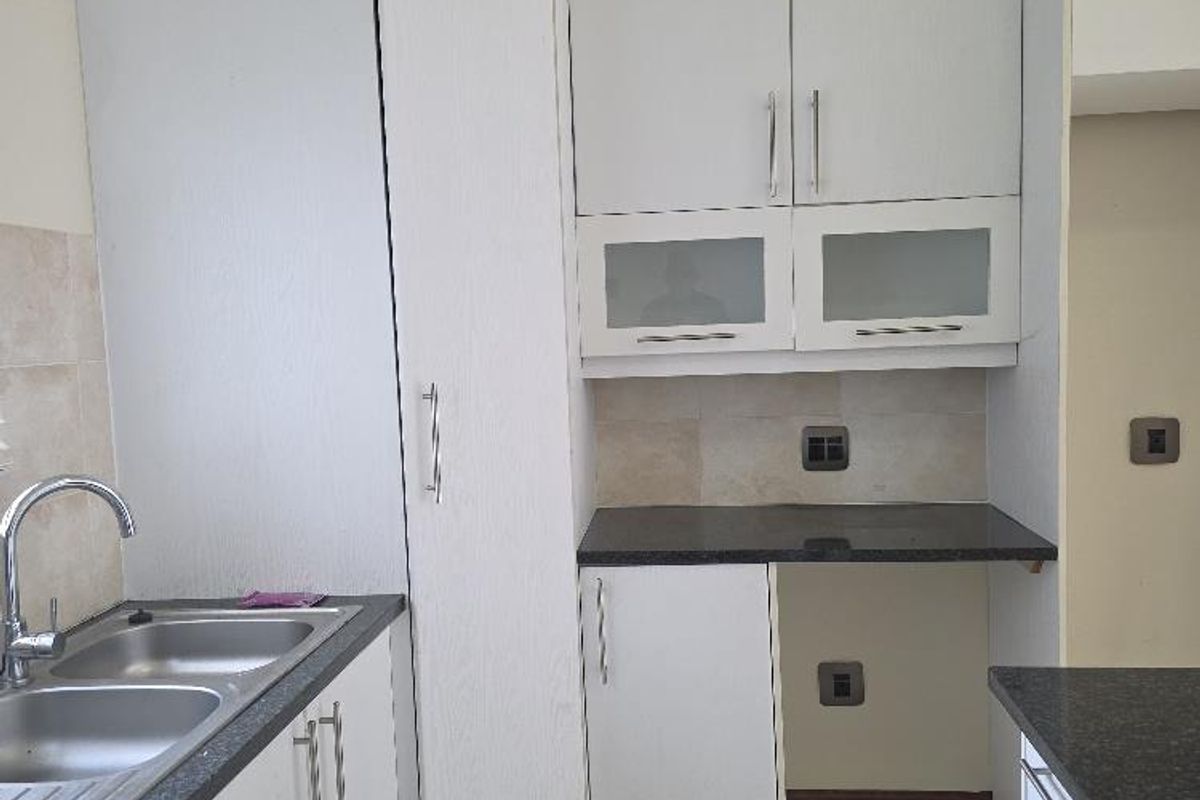 A functional kitchen featuring white cabinetry, dark granite countertops, a double stainless steel sink, and tiled flooring.