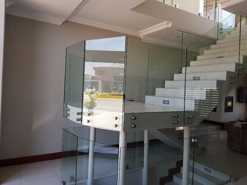 Modern entrance hall featuring a striking glass balustrade staircase with integrated lighting and polished floor tiles.
