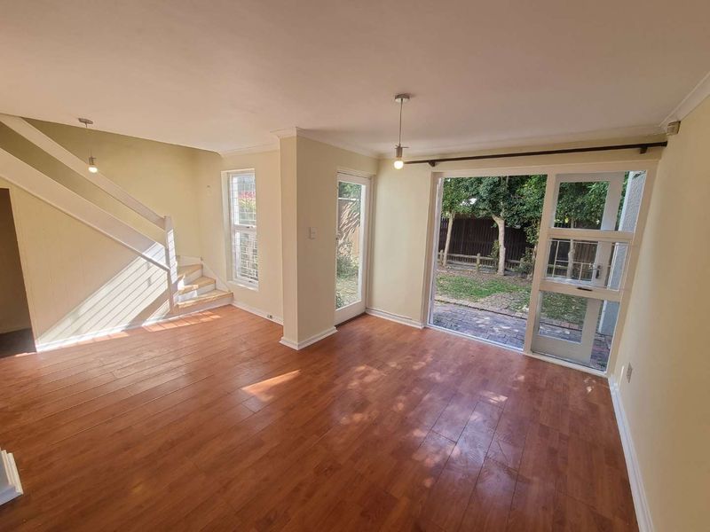 Bright and spacious living area featuring laminate flooring, a staircase, and direct access to the rear garden through sliding glass doors.