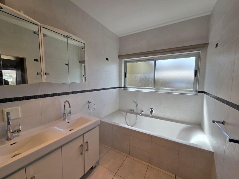 A clean, functional bathroom featuring a double vanity with storage, a built-in bathtub, and tiled finishes throughout.