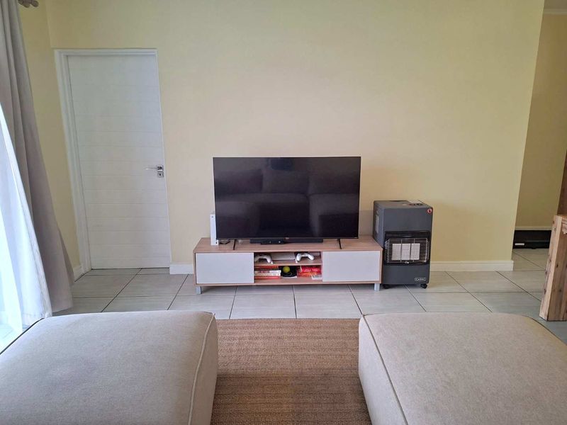 A living room area featuring neutral tiled flooring, a single internal door, and light-colored walls, providing a functional and well-lit space.
