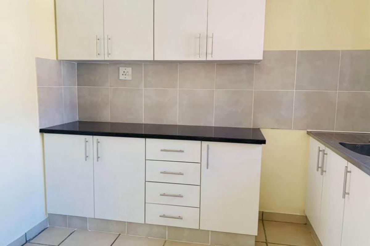 A clean, functional kitchen featuring white built-in cabinetry, dark countertops, neutral tiled backsplash, and ceramic floor tiles.