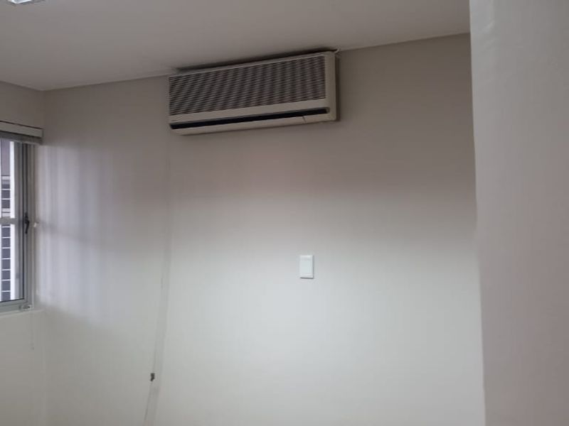 A clean, empty office space featuring a wall-mounted split-system air conditioner and a window with security bars.