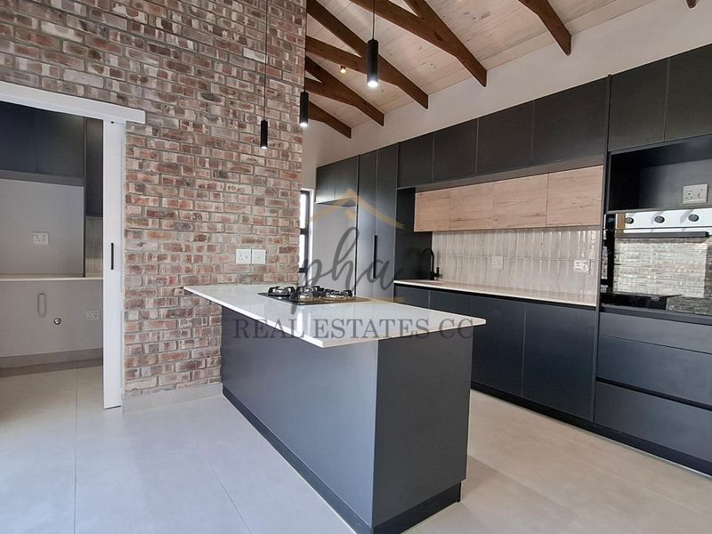 Modern kitchen featuring an island with gas hob, built-in oven, exposed brick feature wall, and vaulted timber ceiling with contemporary pendant lighting.