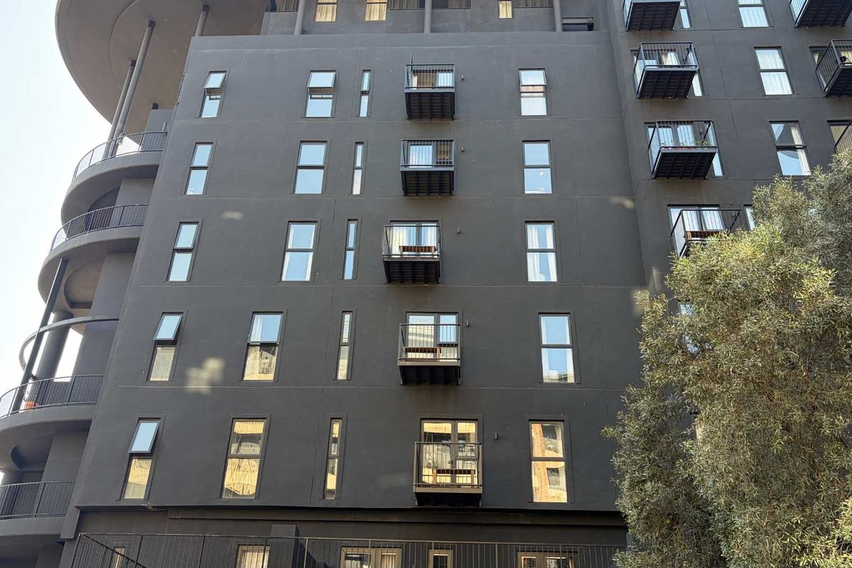 A modern multi-story apartment building facade featuring dark exterior finishes, multiple private balconies with metal railings, and uniform casement windows.