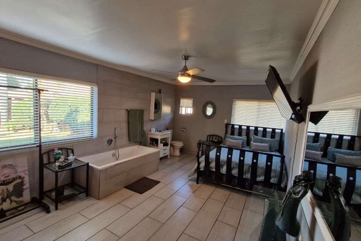 A spacious bedroom featuring an integrated bathtub, tiled flooring, ceiling fan, and neutral wall finishes, offering a unique open-concept layout.