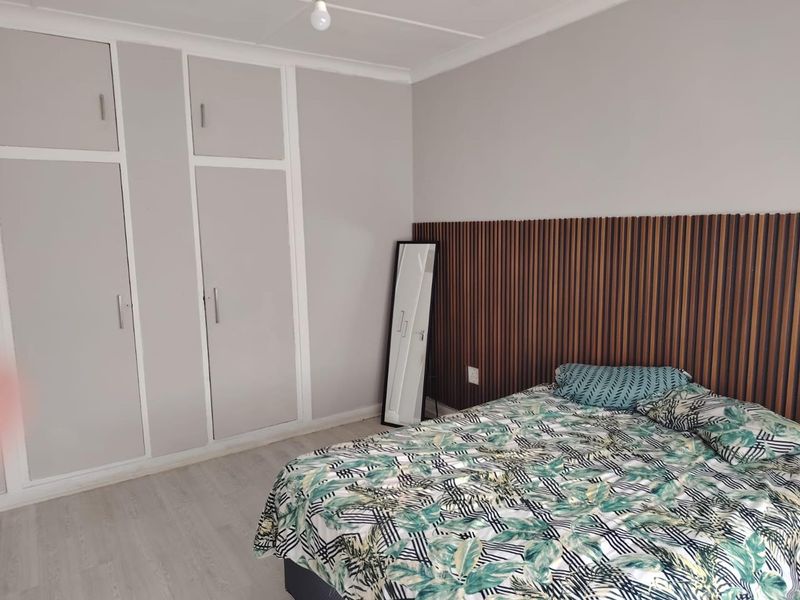 A well-maintained bedroom featuring built-in cupboards, modern laminate flooring, and a decorative slatted wood feature wall behind the bed area.