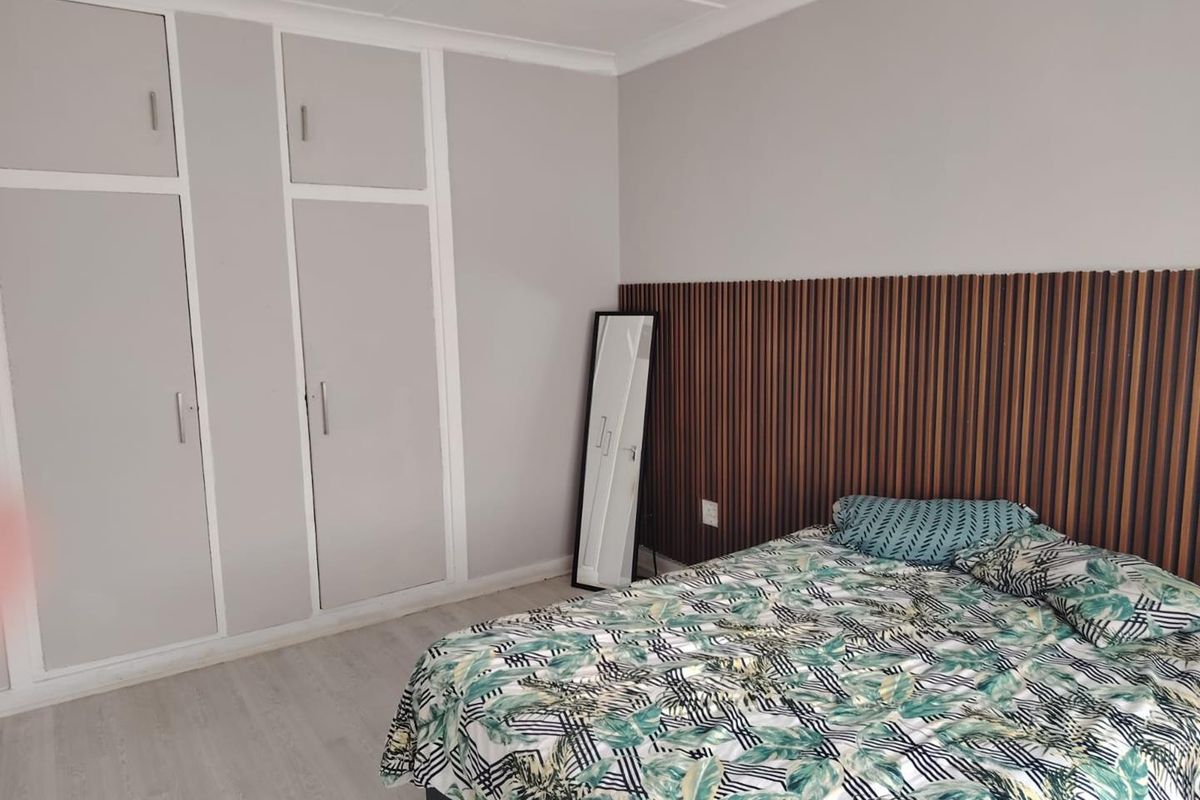 A well-maintained bedroom featuring built-in cupboards, modern laminate flooring, and a decorative slatted wood feature wall behind the bed area.