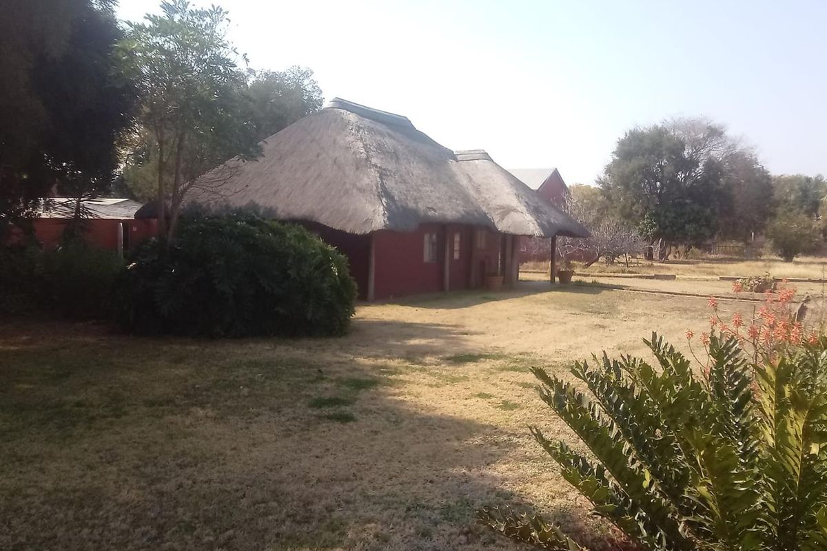 A view of the rear exterior of the property featuring a traditional thatch roof and a covered patio area set within a large garden.
