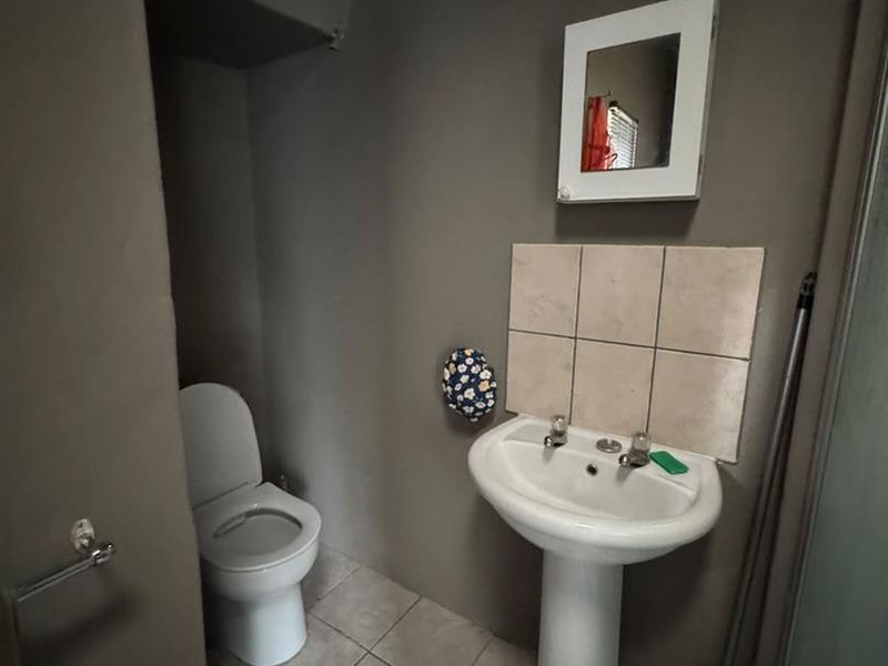 A functional bathroom featuring a pedestal basin, tiled splashback, and a standard toilet with neutral wall finishes and tiled flooring.