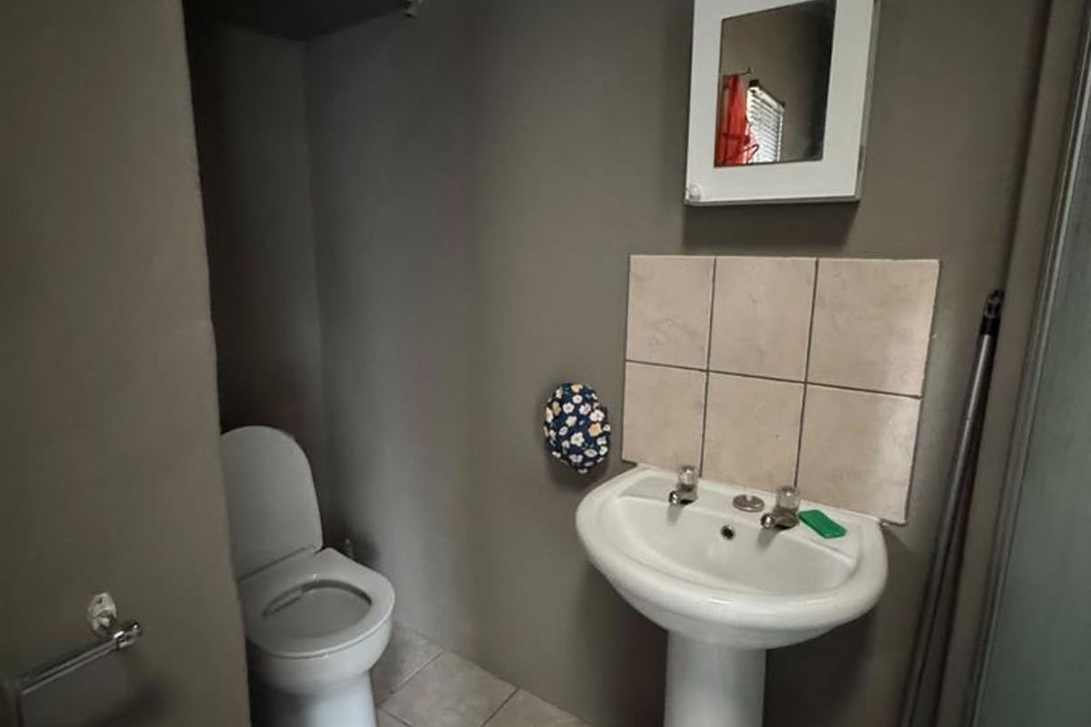 A functional bathroom featuring a pedestal basin, tiled splashback, and a standard toilet with neutral wall finishes and tiled flooring.