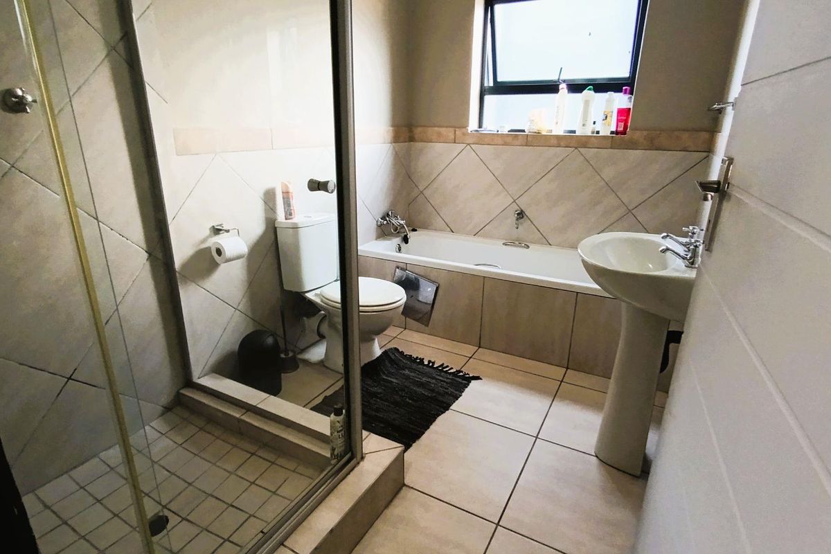 A functional bathroom featuring a separate shower enclosure, a bathtub, a pedestal basin, and a toilet with neutral wall and floor tiling.