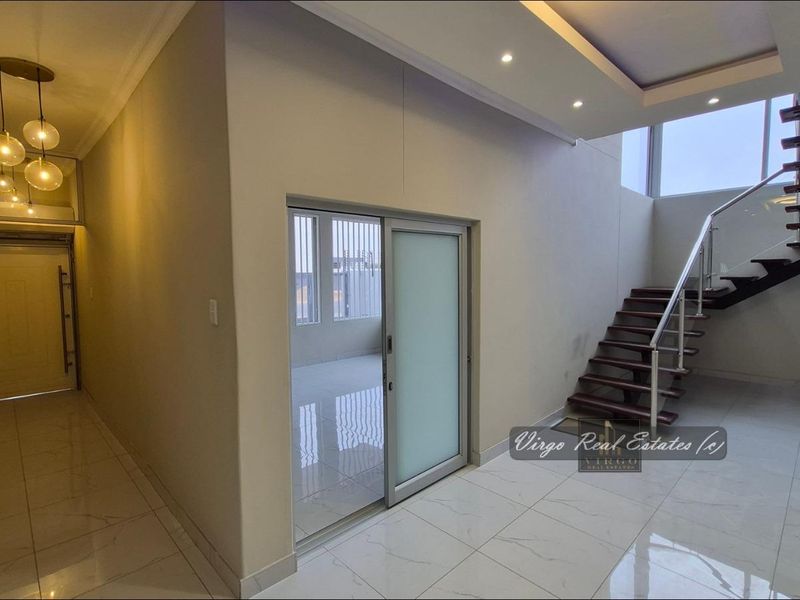 Spacious entrance hall featuring modern tiled flooring, a contemporary staircase with glass balustrade, and recessed ceiling lighting.