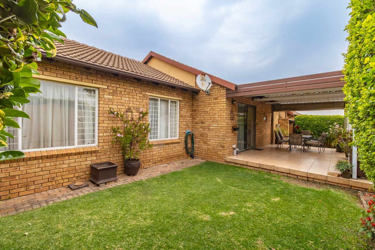 Rear view of the townhouse featuring a brick facade, a covered patio area, and a well-maintained lawn.