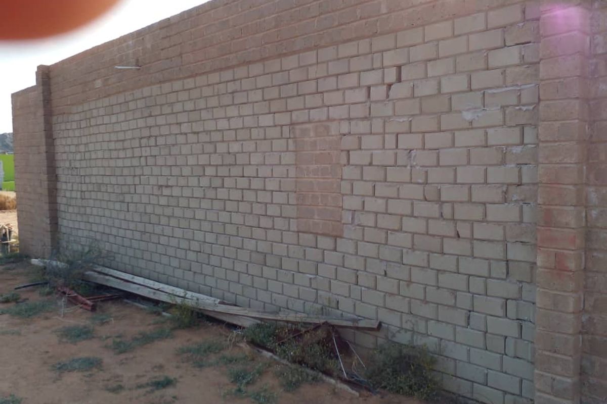 A view of an exterior brick boundary wall showing signs of structural cracking and a previously infilled opening.