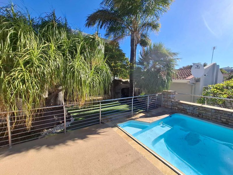 Outdoor pool area featuring a swimming pool, stone-clad retaining wall, stainless steel balustrade, and landscaped garden area with artificial lawn.