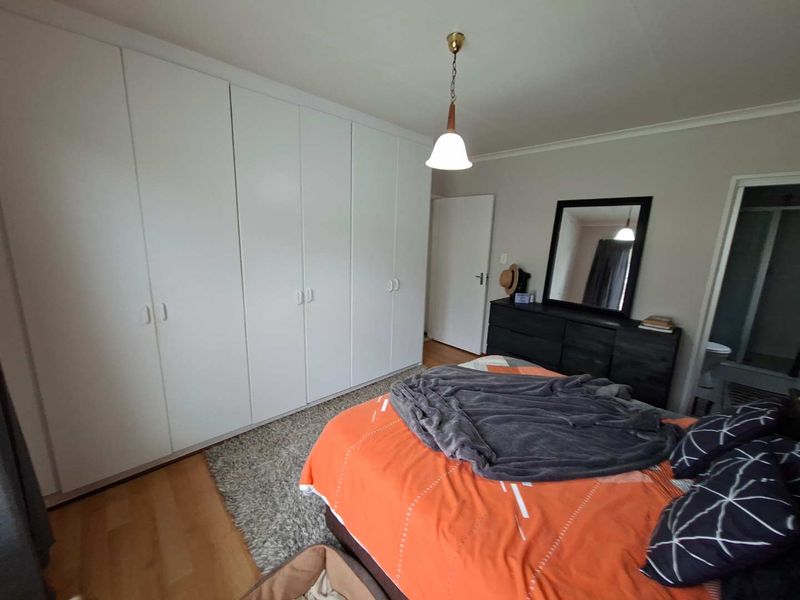 A well-maintained bedroom featuring extensive floor-to-ceiling built-in wardrobes, laminate flooring, and a classic pendant light fixture.