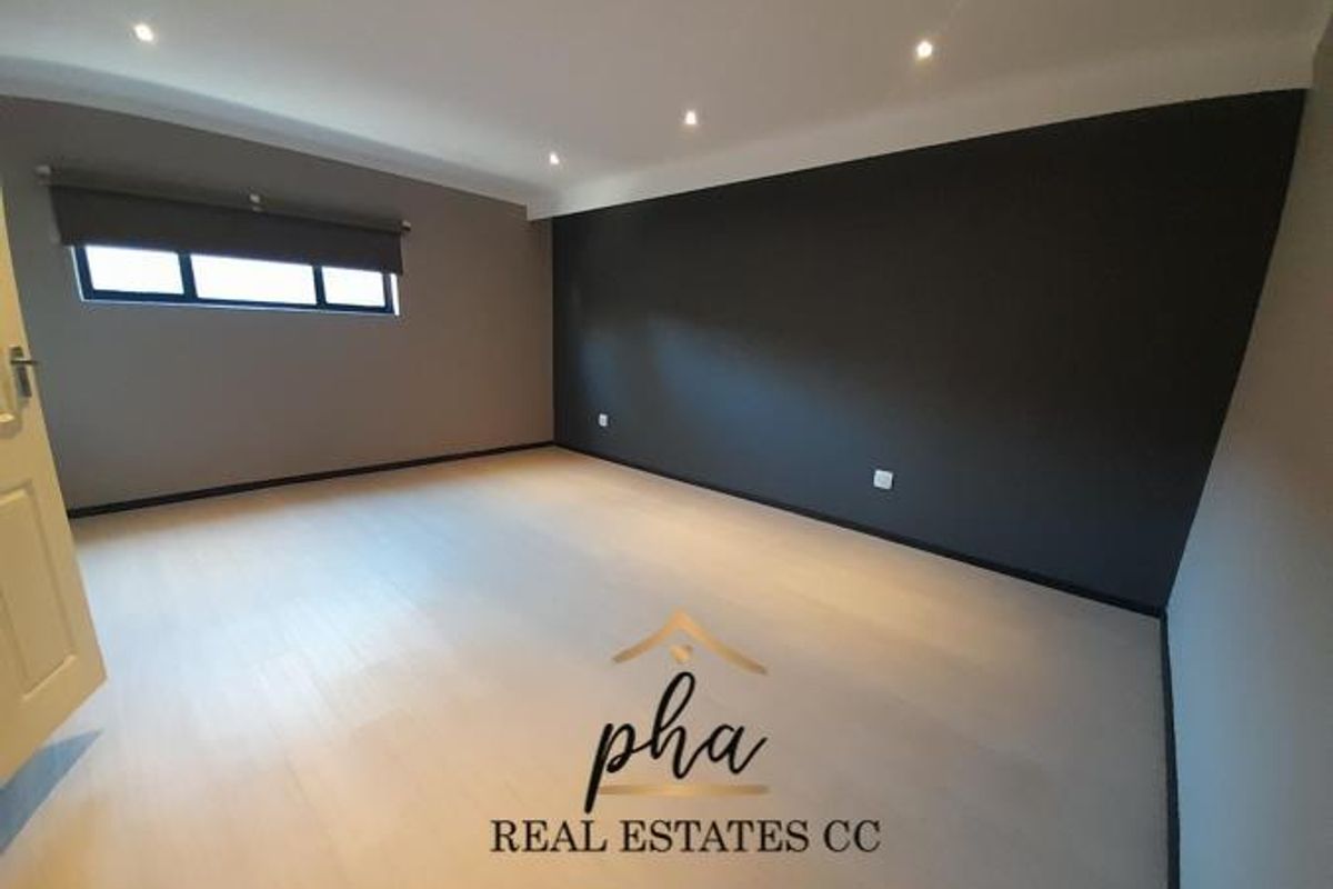 A spacious, empty bedroom featuring modern recessed ceiling lighting, light-toned laminate flooring, and a striking dark accent wall.