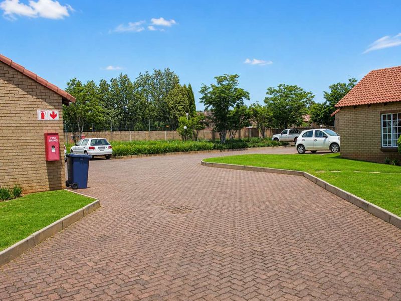 A view of the complex driveway featuring brick paving, manicured lawns, and face brick townhouse exteriors with tiled roofs.