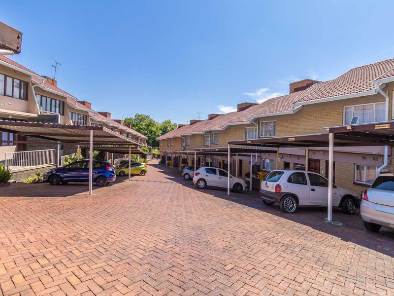 Exterior view of an apartment complex featuring a paved driveway, covered parking bays, and brick-faced residential units with tiled roofing.