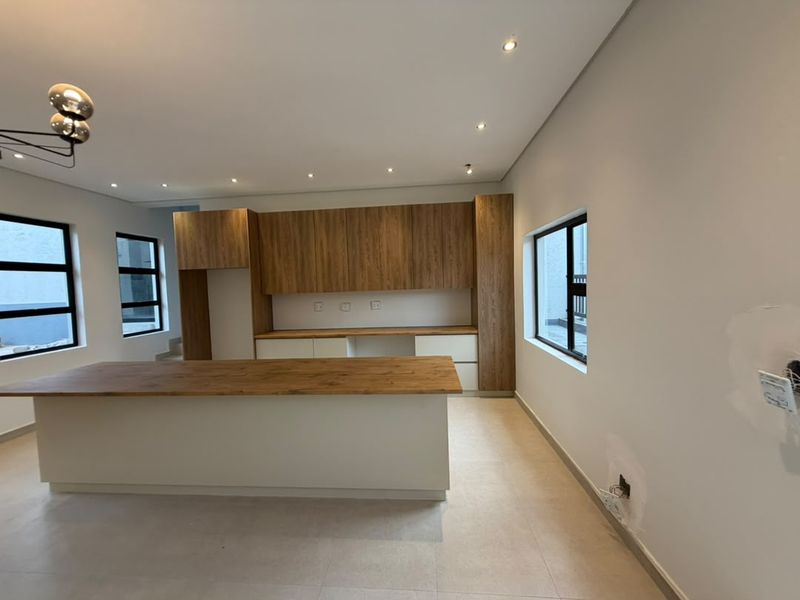 Modern kitchen featuring a central island, wood-finish cabinetry, and tiled flooring. The space is currently vacant and requires minor finishing touches to the walls.