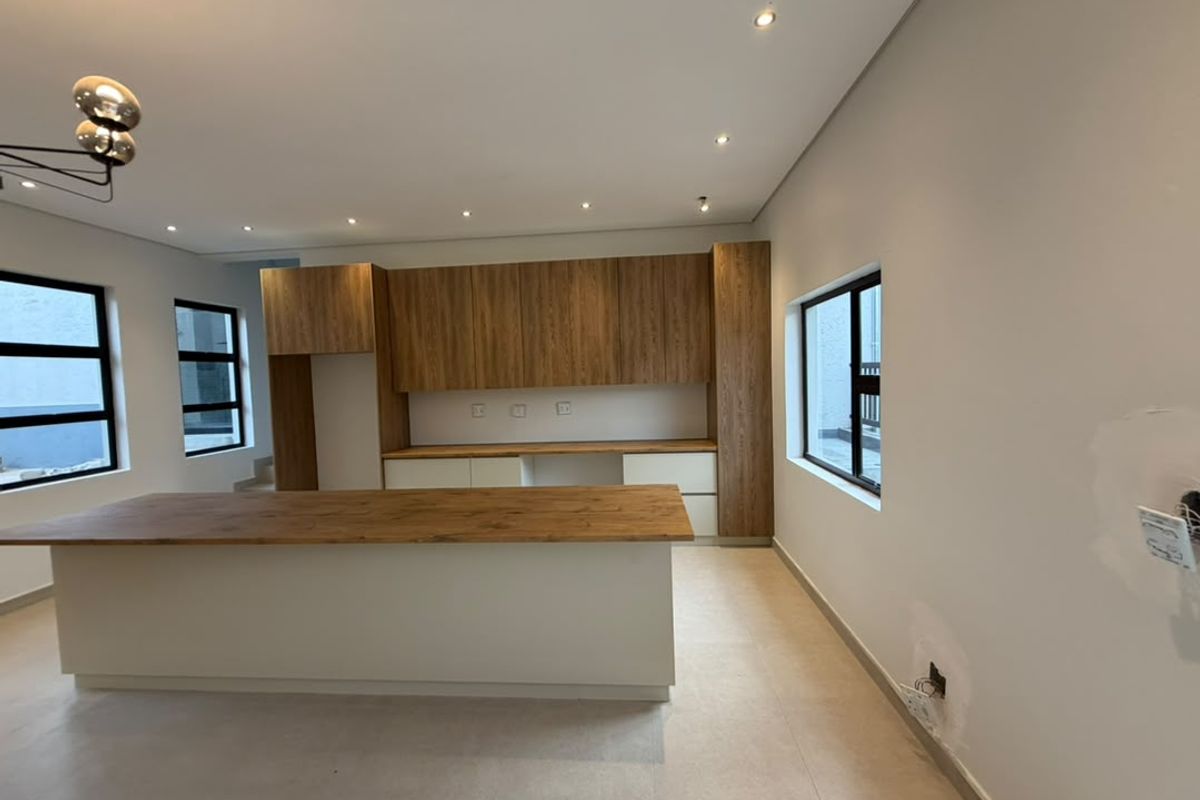 Modern kitchen featuring a central island, wood-finish cabinetry, and tiled flooring. The space is currently vacant and requires minor finishing touches to the walls.