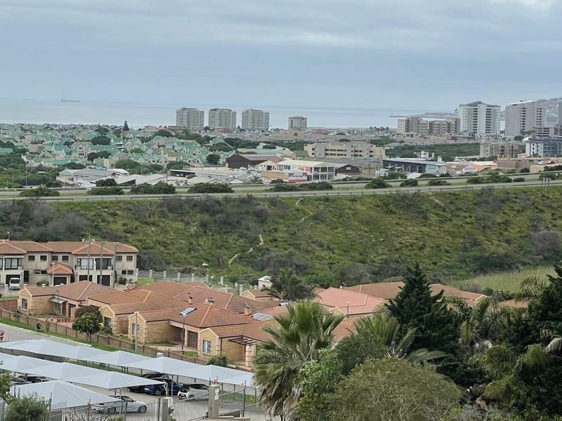 An elevated panoramic view overlooking a residential neighborhood, coastal landscape, and distant urban development under an overcast sky.